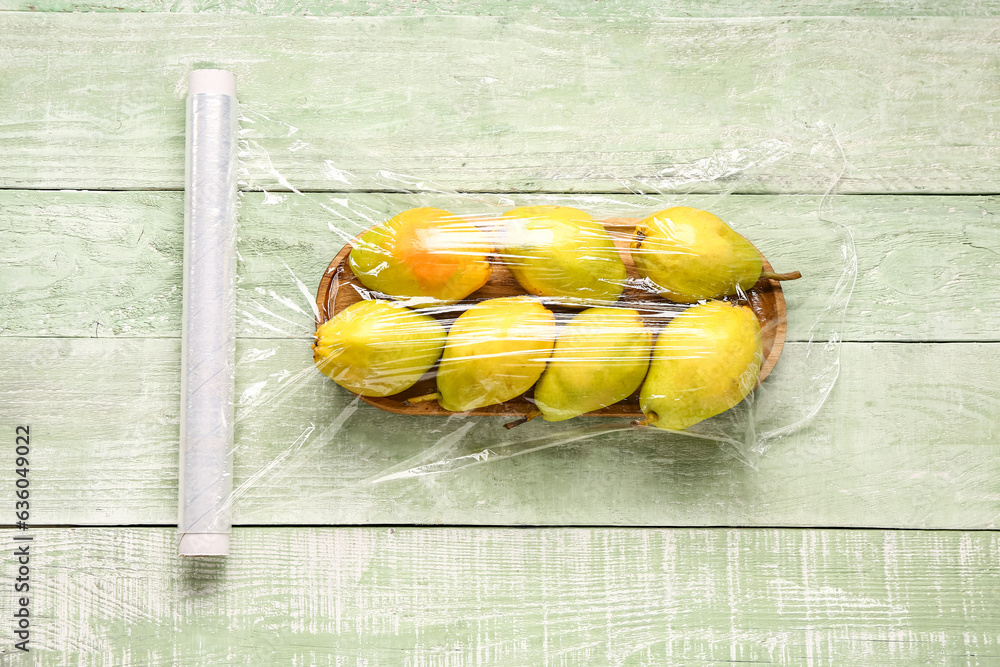 Board of fresh pears covered with plastic food wrap on green wooden background