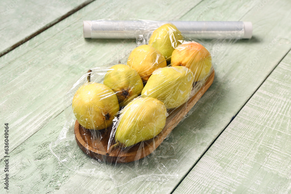 Board of fresh pears covered with plastic food wrap on green wooden background