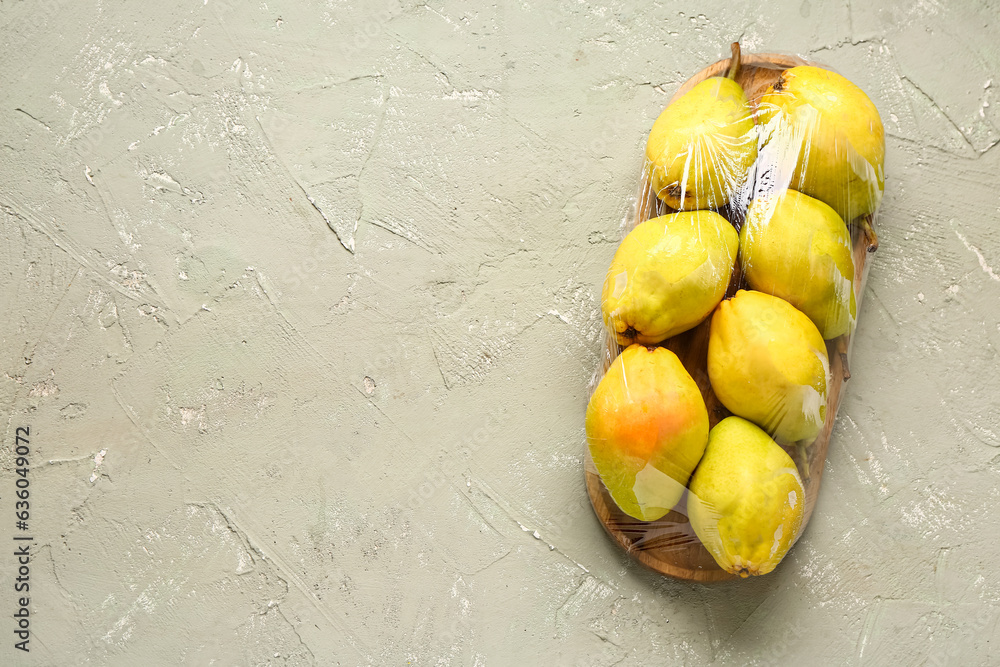 Wooden board of fresh pears covered with plastic food wrap on grey background