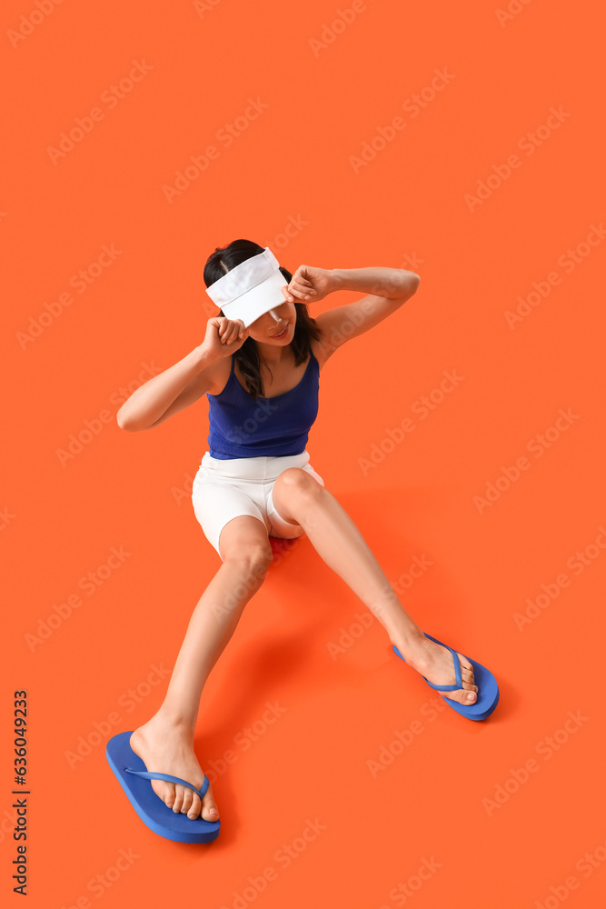 Pretty Asian woman in beachwear on orange background