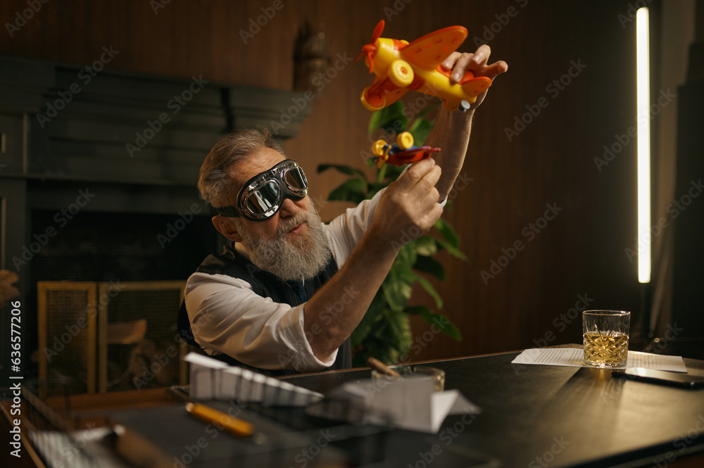 Playful senior boss or businessman playing toy plane at work table