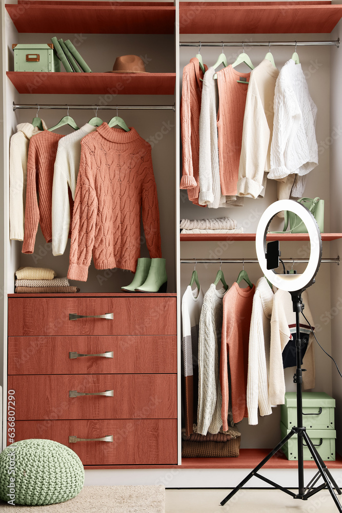 Ring lamp and warm sweaters hanging in wooden wardrobe