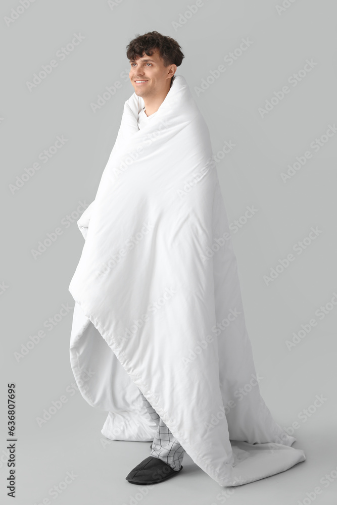 Handsome happy man wrapped in soft blanket on grey background