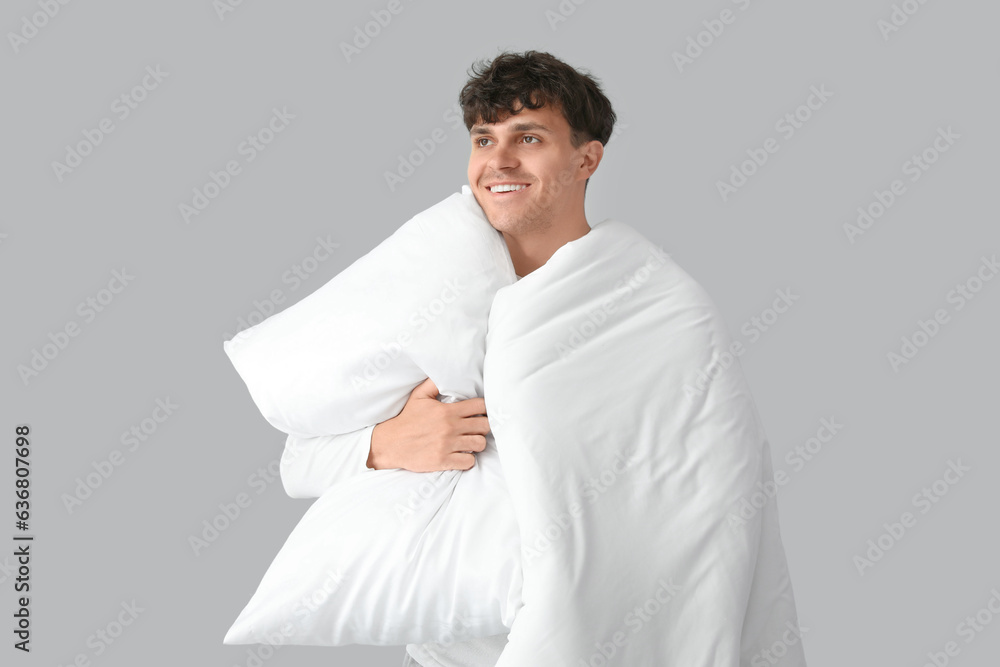 Handsome happy man with soft blanket and pillow on grey background