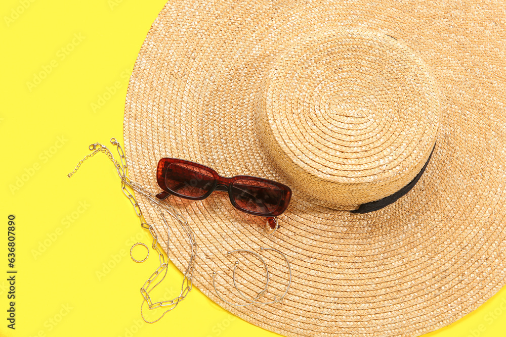 Stylish sunglasses with hat and jewellery on yellow background