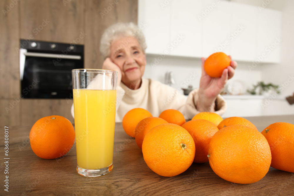 Glass of juice with oranges on table in kitchen, closeup