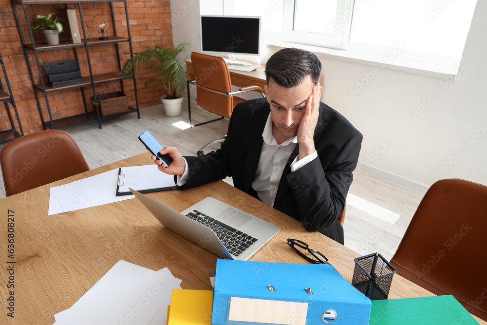 Stressed businessman with mobile phone working under deadline in office