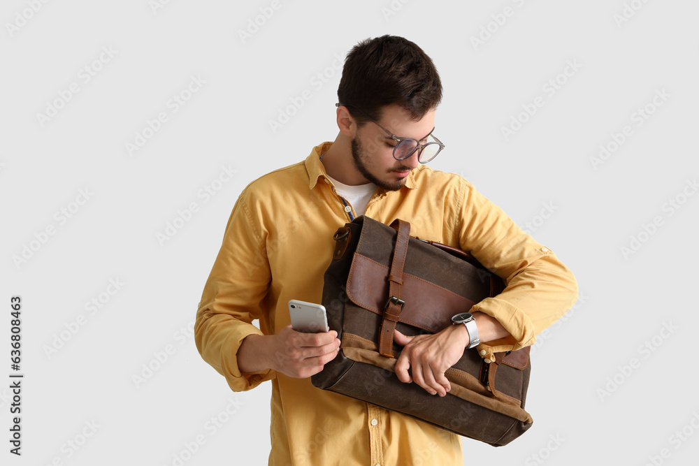 Stressed young man with briefcase and mobile phone looking at wristwatch on light background. Deadli