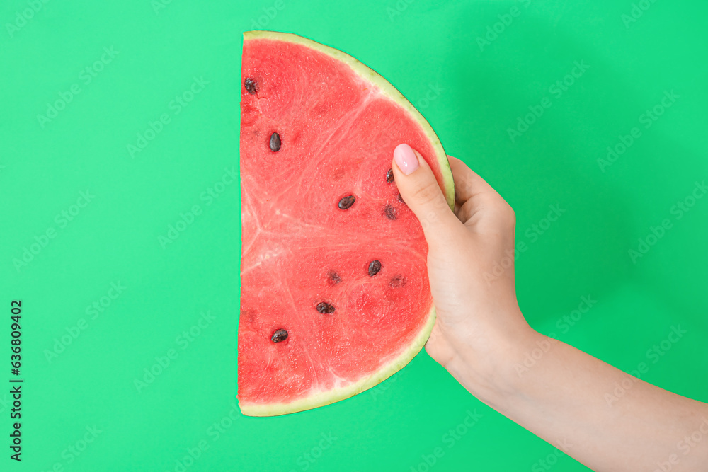 Female hand with piece of ripe watermelon on green background