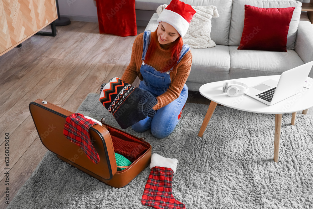 Young woman unpacking suitcase at home on Christmas holidays