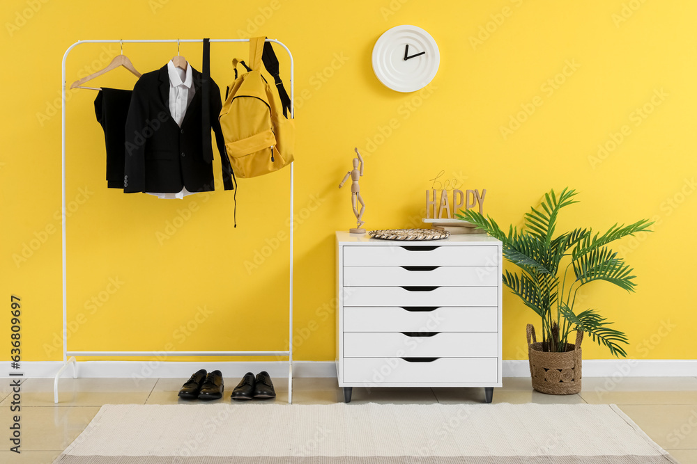 Rack with stylish school uniform and backpack near yellow wall in room