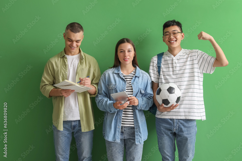 Happy students with notebooks, tablet and soccer ball on green background