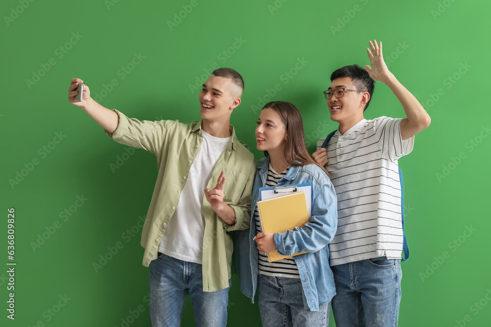 Happy students with notebooks taking selfie on green background