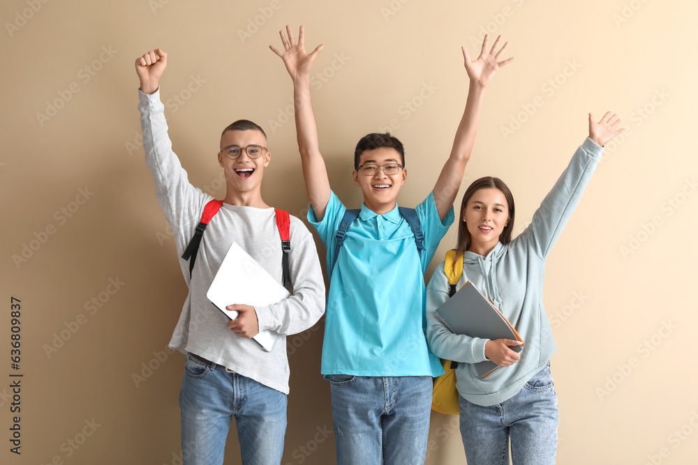 Happy students with backpacks, notebooks and laptop on beige background