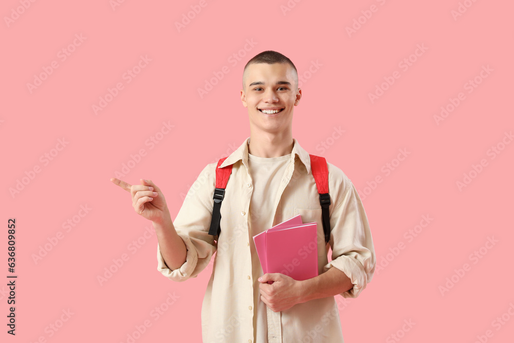 Happy male student with backpack and notebooks pointing at something on pink background