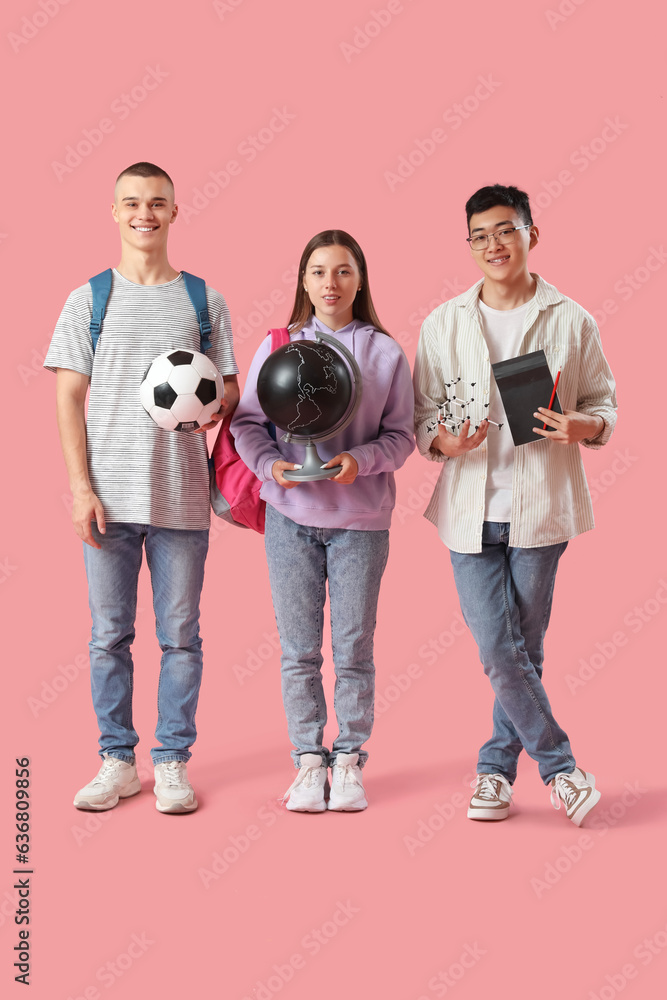 Happy students with soccer ball, globe and molecular model on pink background