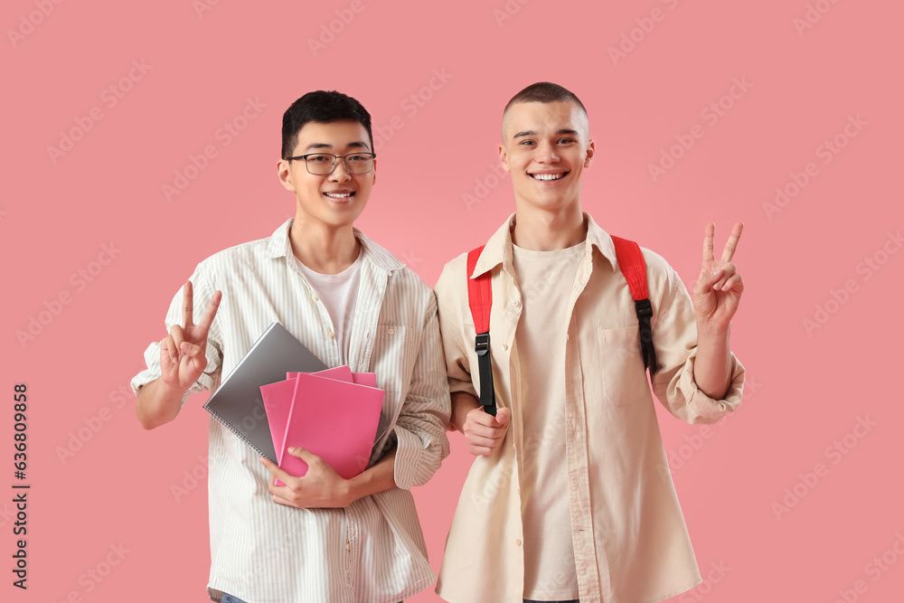 Happy students with notebooks showing victory gesture on pink background