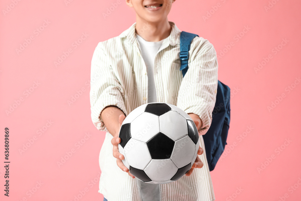 Happy male Asian student with backpack and soccer ball on pink background