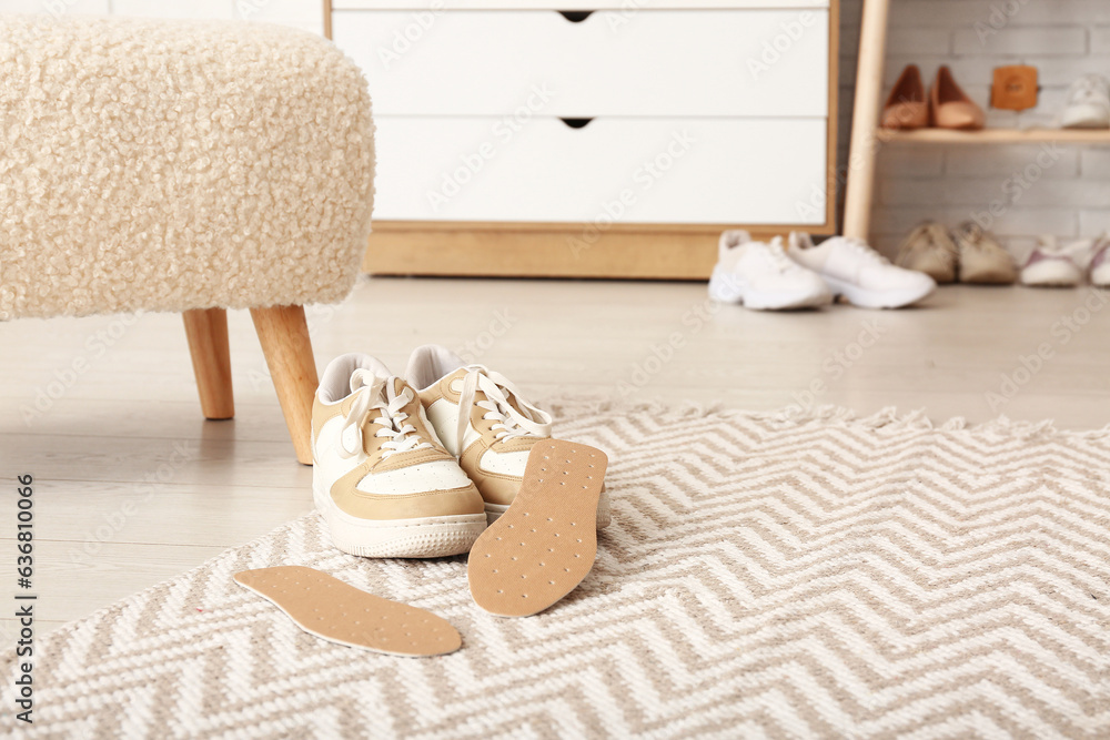 Stylish sneakers with orthopedic insoles and stool on floor in room