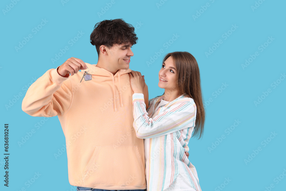 Young couple with key from house on blue background