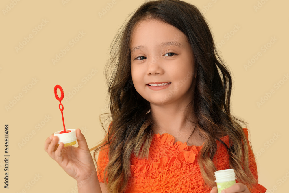 Cute little girl blowing soap bubbles on beige background