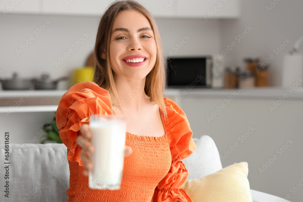 Young woman with glass of milk sitting on sofa