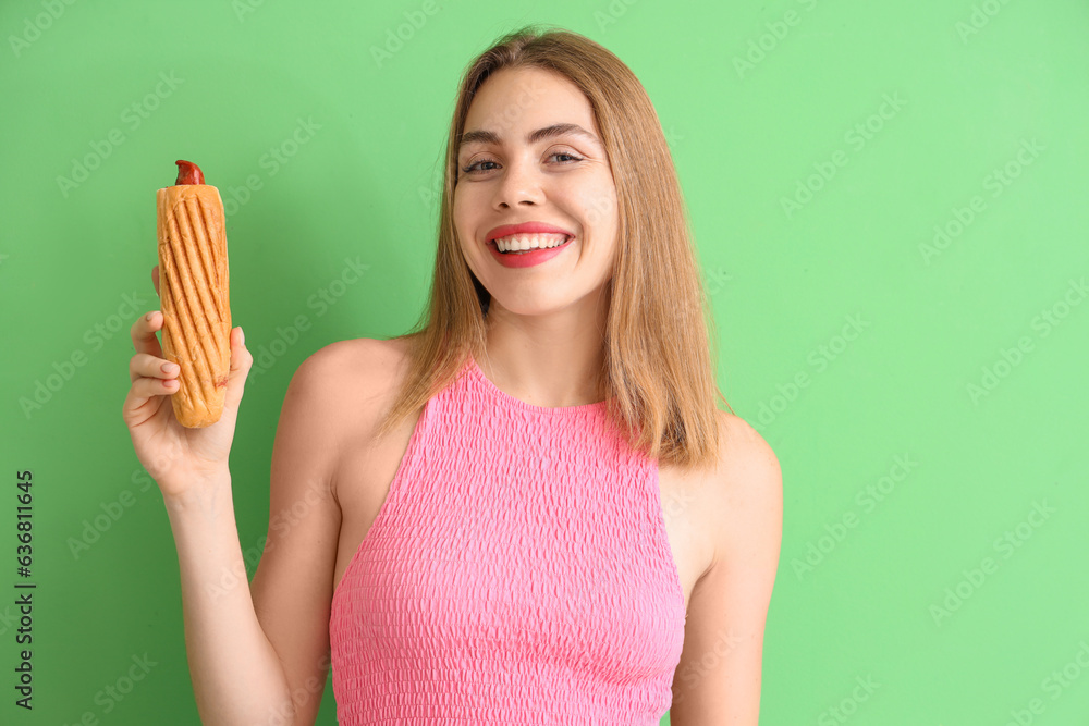 Pretty young woman with tasty hot dog on green background