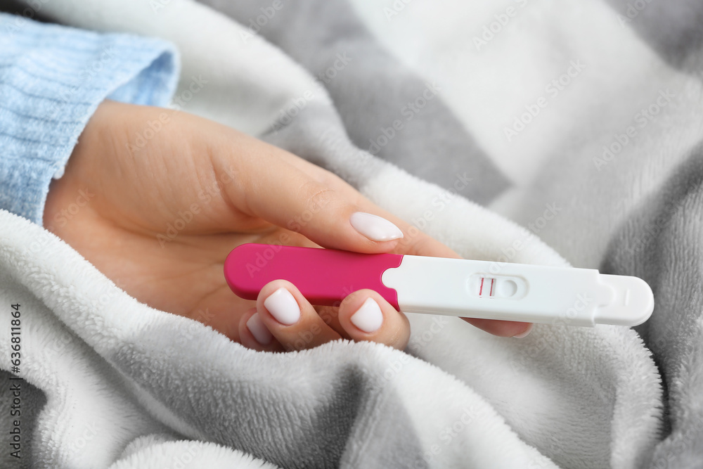 Female hand with positive pregnancy test on plaid, closeup