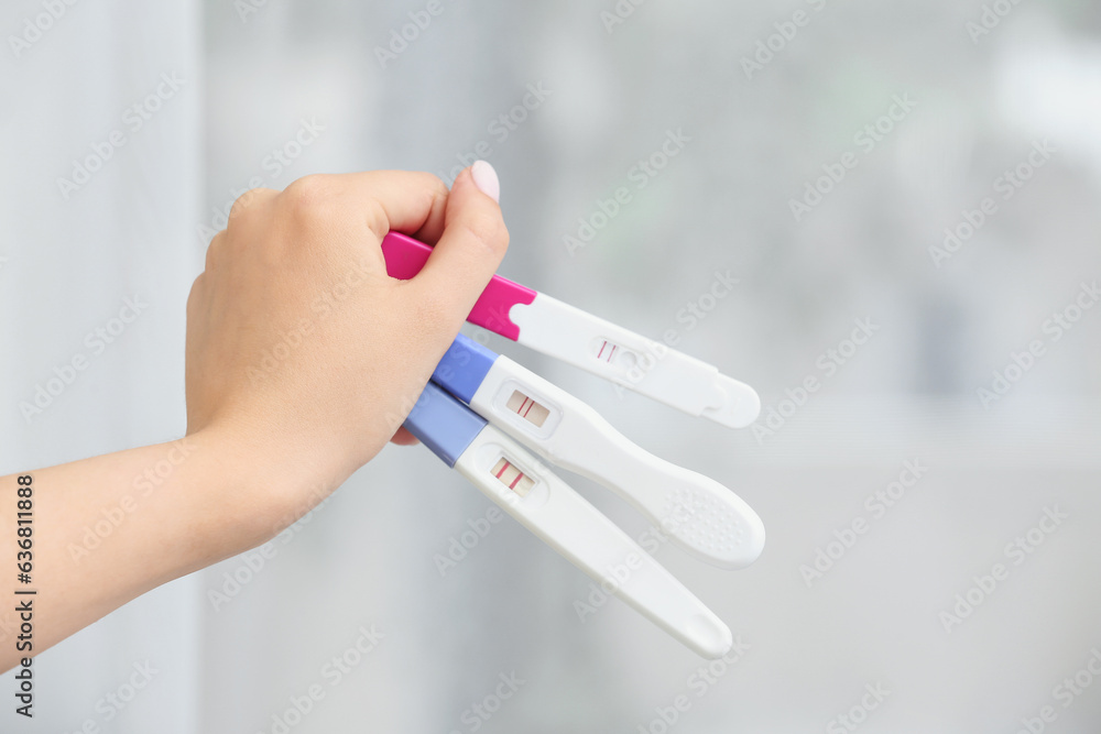 Female hand with positive pregnancy tests on blurred background, closeup