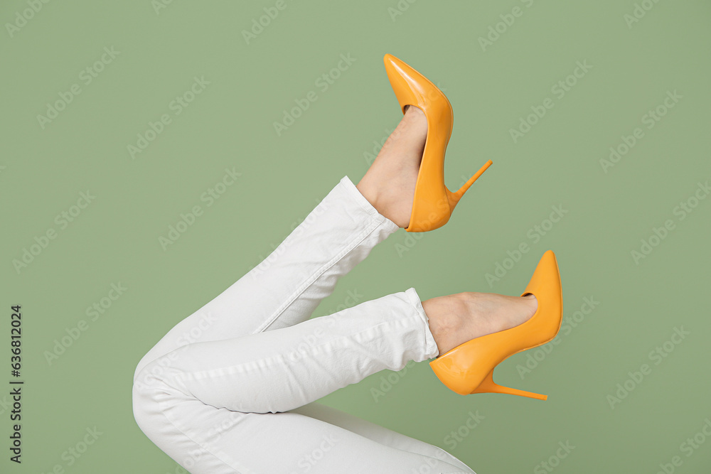 Female legs in stylish high heeled shoes on green background