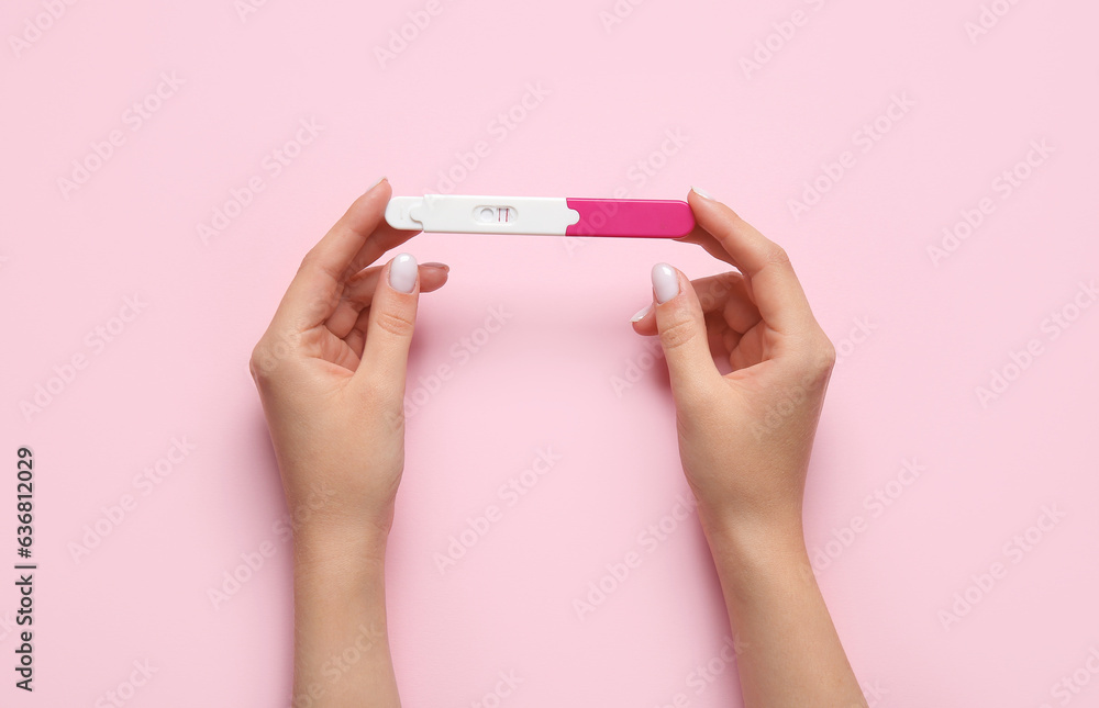 Female hands with pregnancy test on pink background