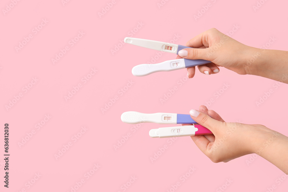 Female hands with different pregnancy tests on pink background