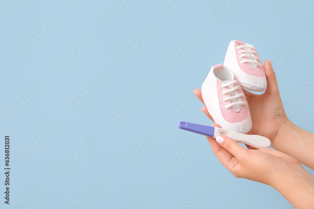 Female hands with positive pregnancy test and baby booties on color background