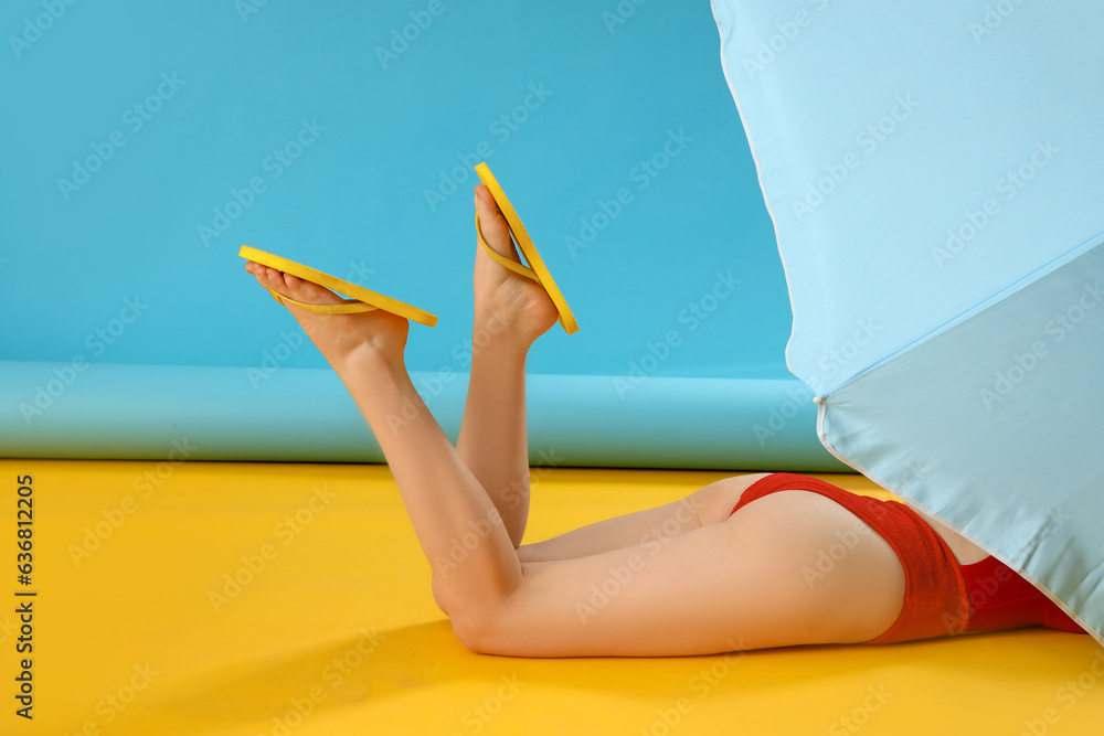 Female legs in stylish flip flops with umbrella on color background