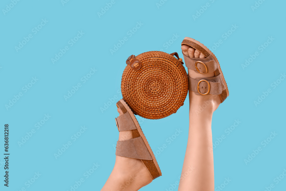 Female legs in stylish sandals with wicker bag on blue background