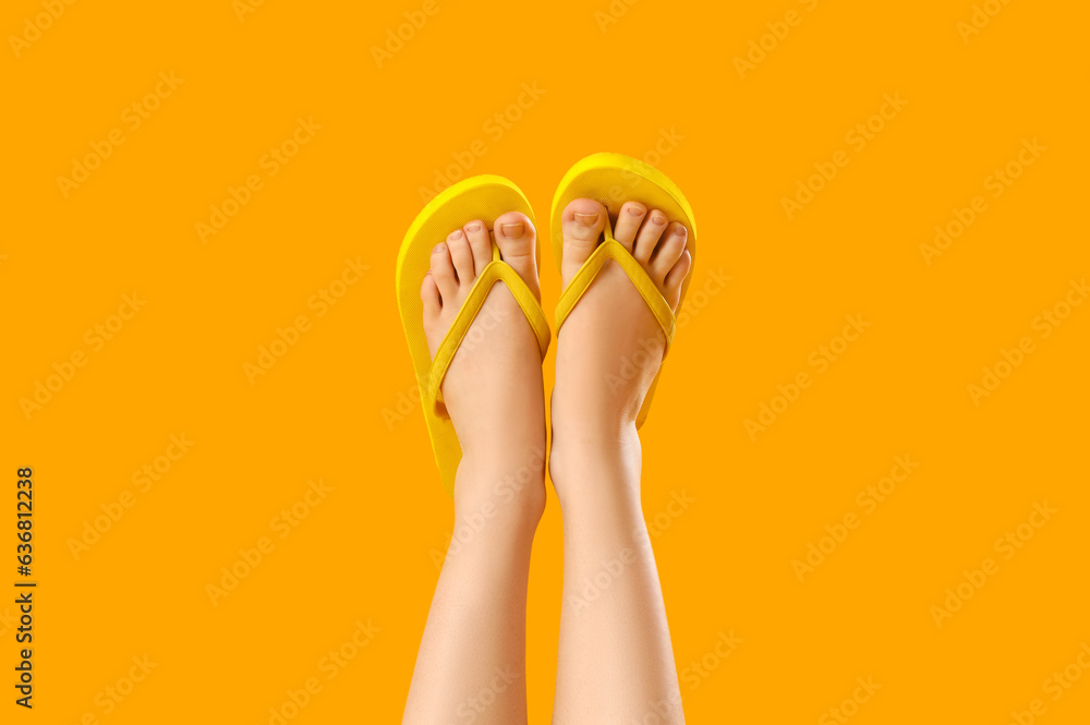 Female legs in stylish flip flops on yellow background