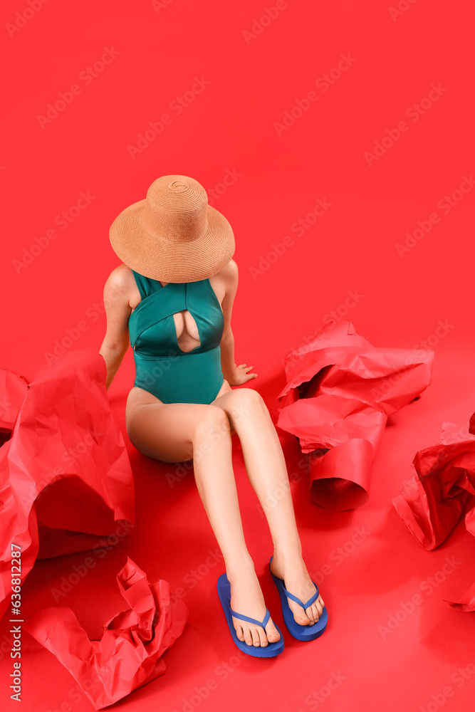 Beautiful young woman in stylish flip flops sitting on red background