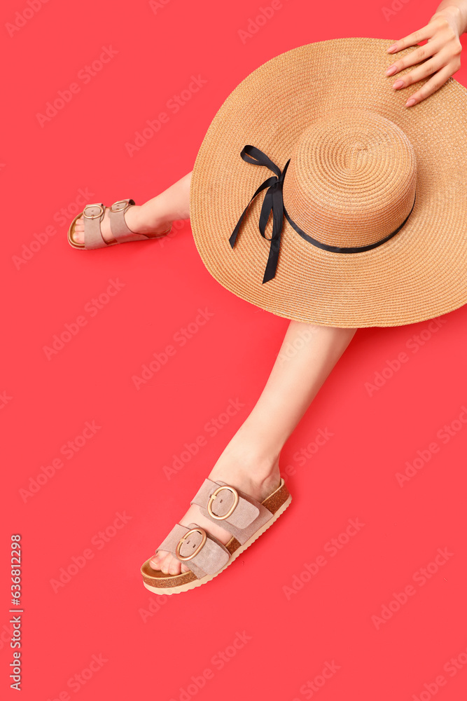 Female legs in stylish sandals with wicker hat on red background