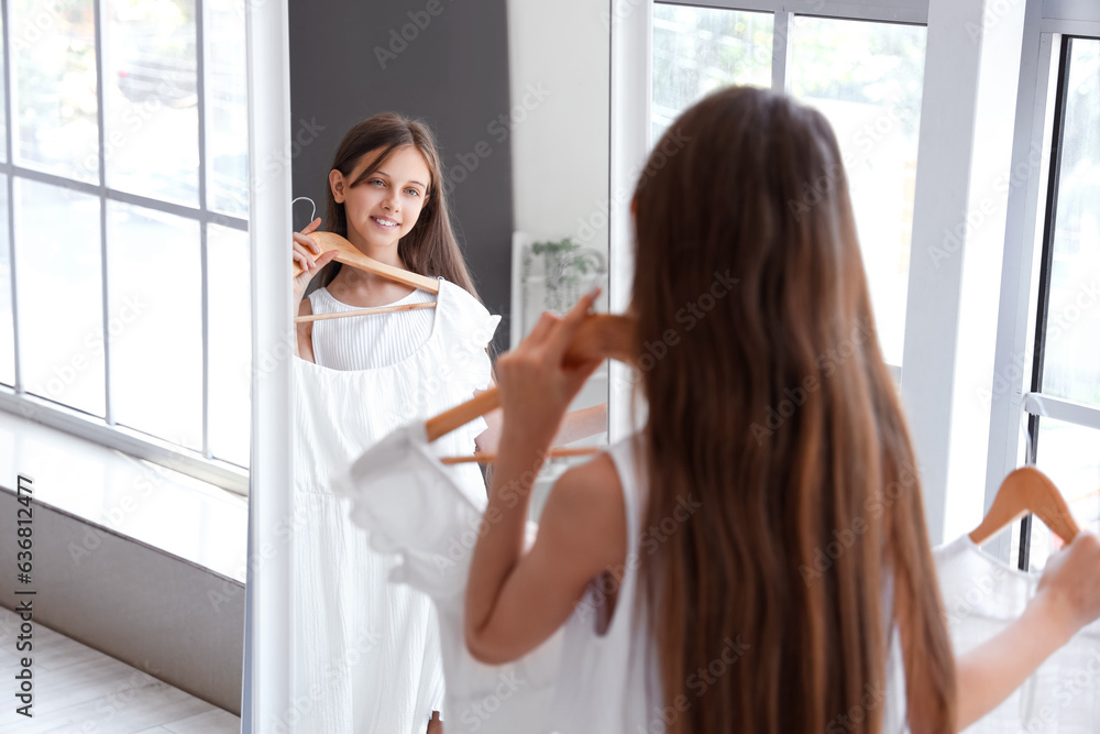 Happy little girl with new dress looking in mirror at home