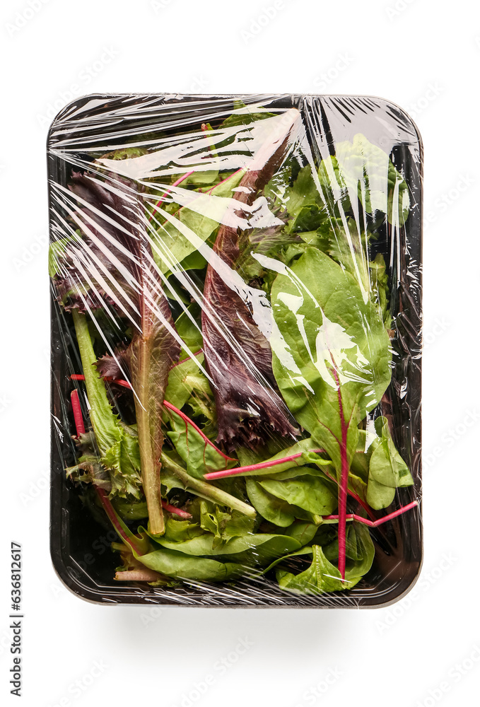 Fresh salad leaves covered with plastic food wrap on white background