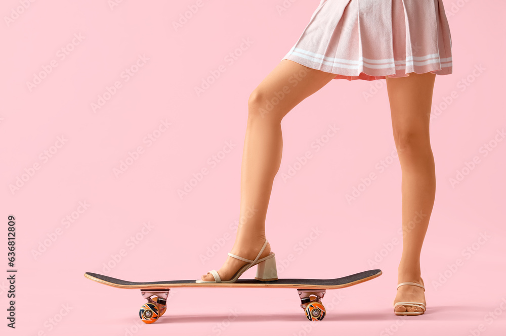 Legs of young woman with skateboard on pink background