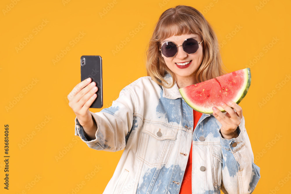 Young woman with fresh watermelon taking selfie on orange background