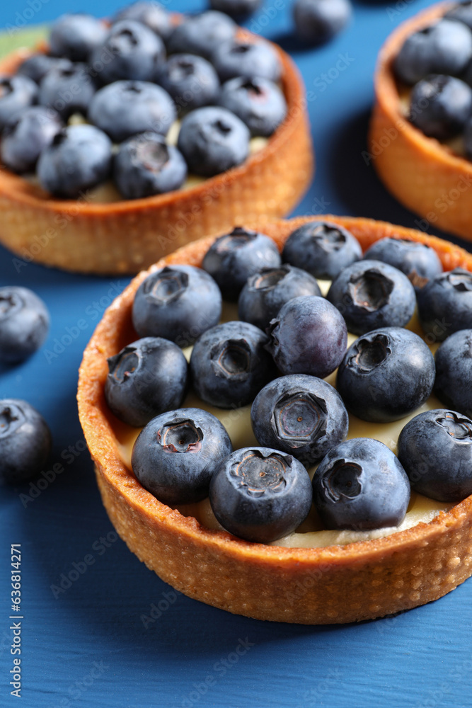 Tartlets with fresh blueberries on blue table, closeup. Delicious dessert