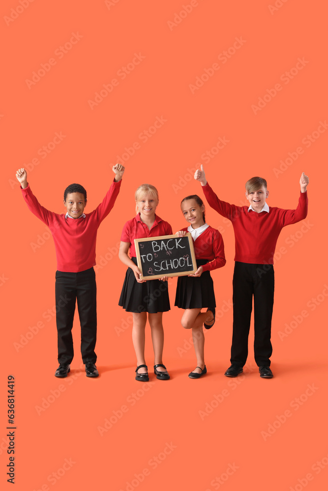 Little classmates in stylish uniform holding blackboard with text BACK TO SCHOOL on orange backgroun