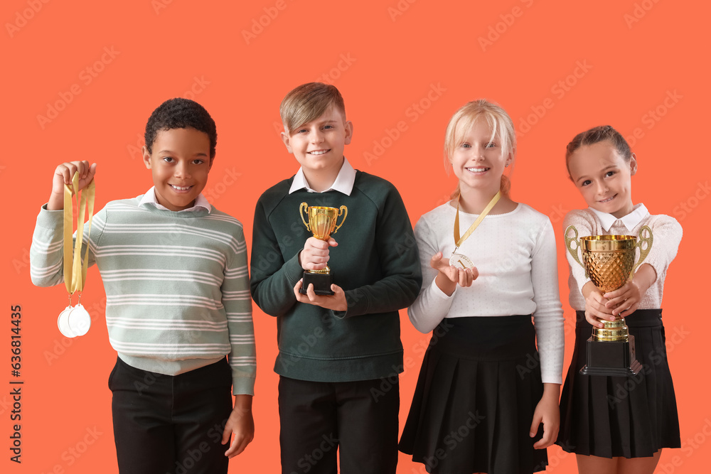 Smart little classmates in stylish uniform with prize cups and medals on orange background