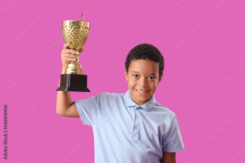 Smart African-American schoolboy in stylish uniform with prize cup on purple background