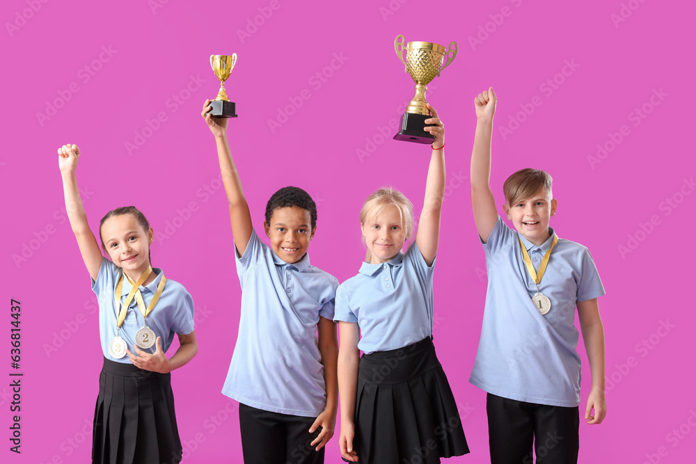 Smart little classmates in stylish uniform with prize cups and medals on purple background