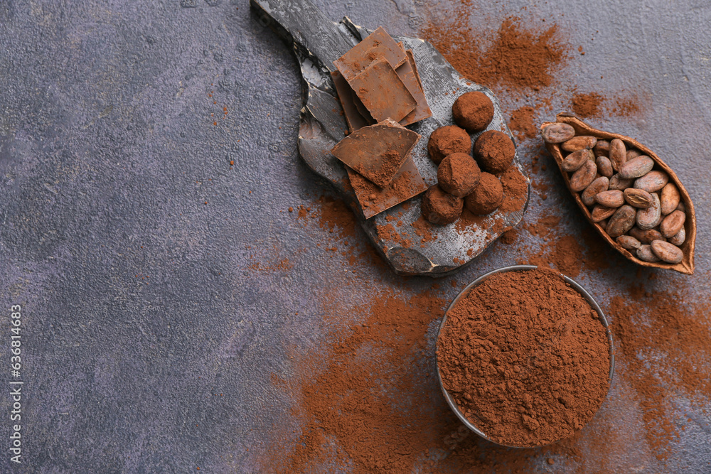 Bowl with cocoa powder, candies, beans and chocolate on black background