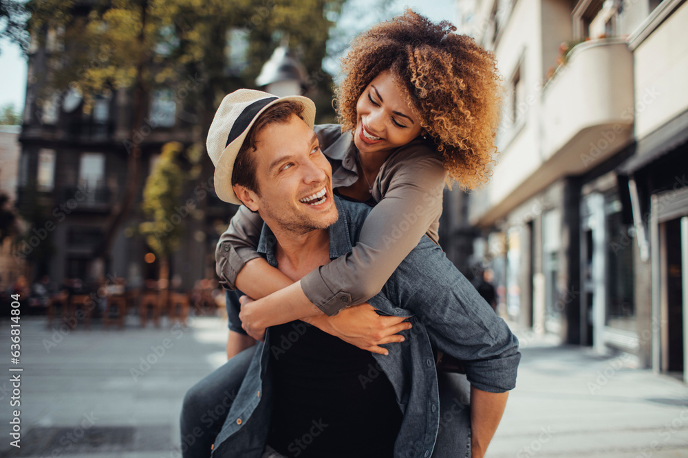 Young man carrying his girlfriend on his back while on a date in the city