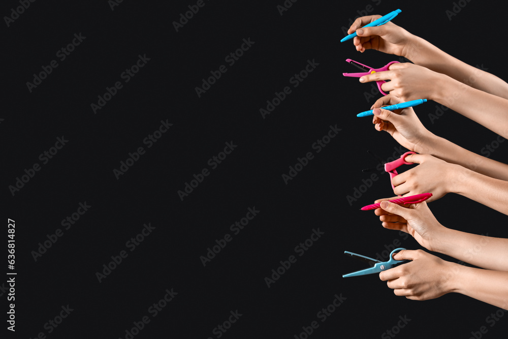 Many female hands with different pens and scissors on black background